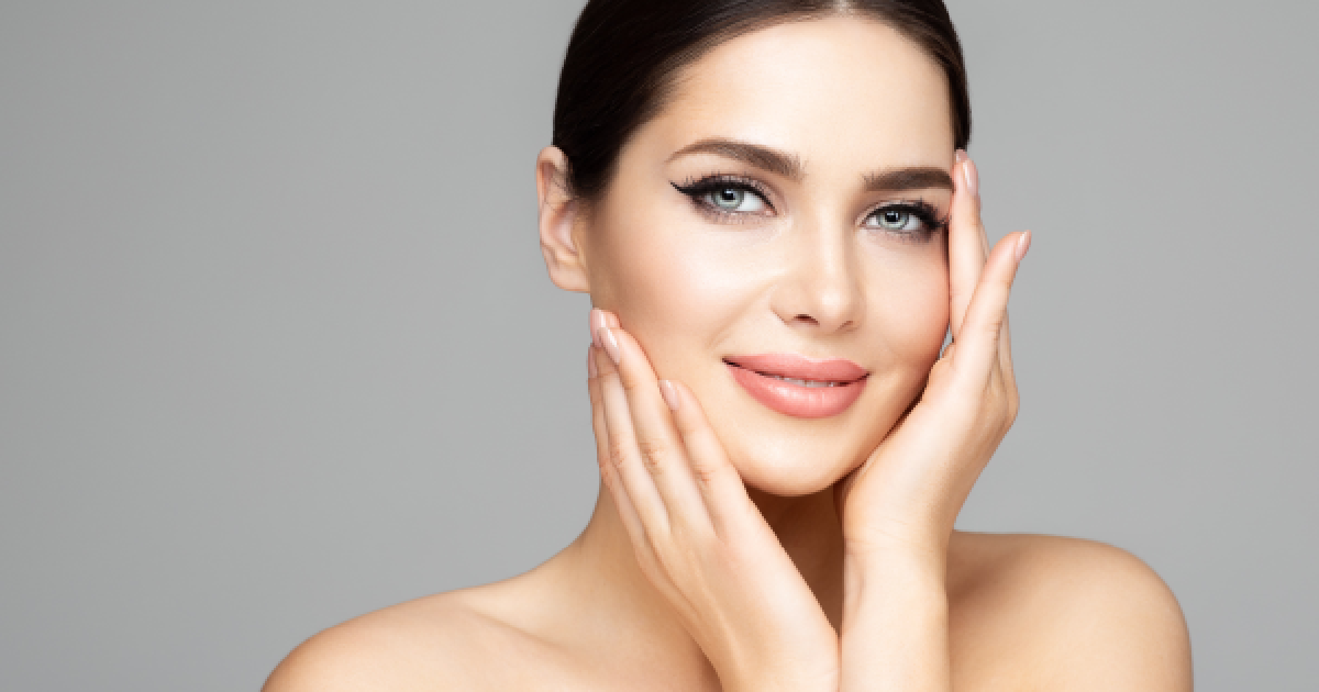 Smiling woman with flawless skin touching her face gently, showcasing smooth, youthful complexion after Sculptra treatment in Kalispell, MT.